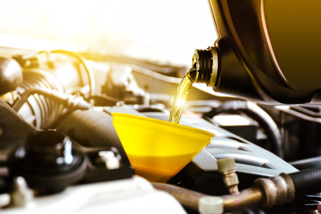 Mechanic pouring engine oil into a car with sunlit background